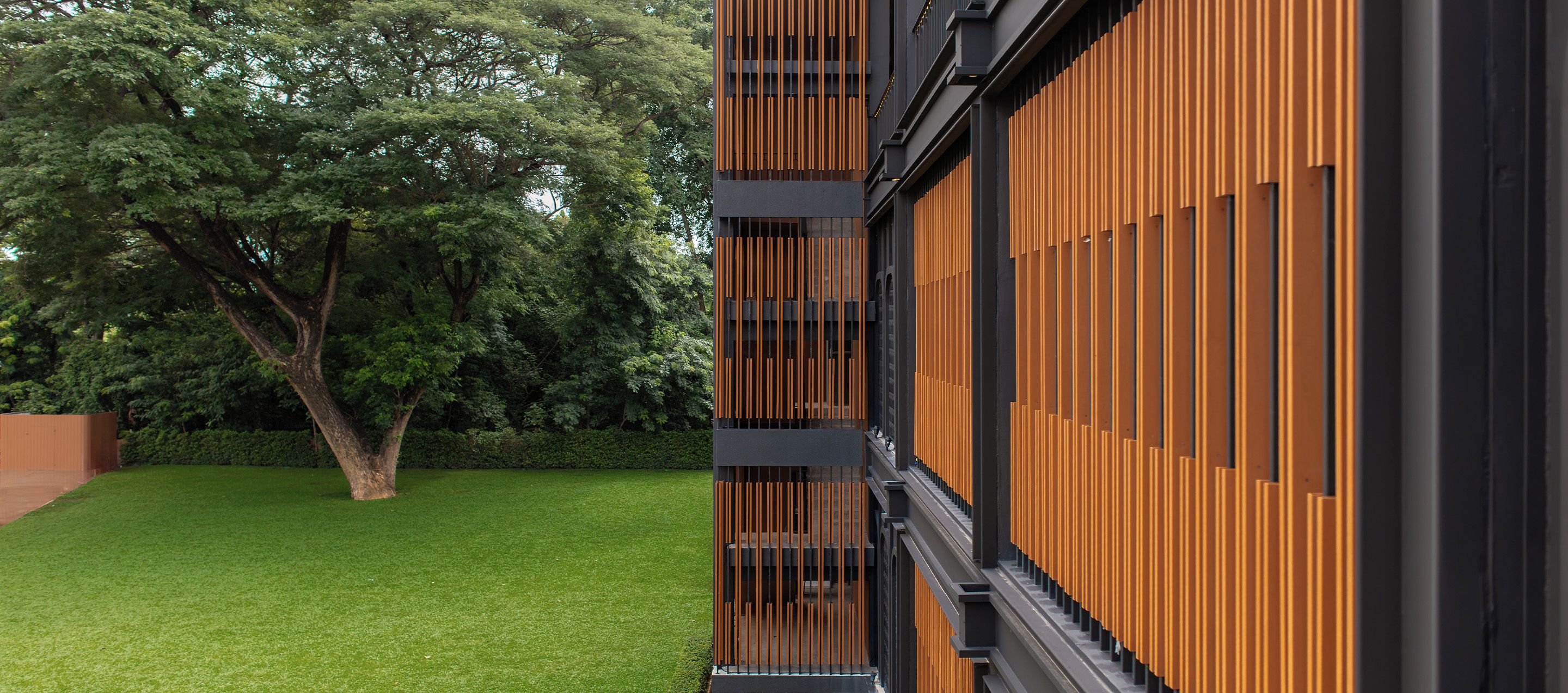 A modern building with a vertical wooden facade and a well-maintained lawn.