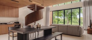 A modern kitchen with a central island, a dining area with a bench, and a large window offering a view of greenery.