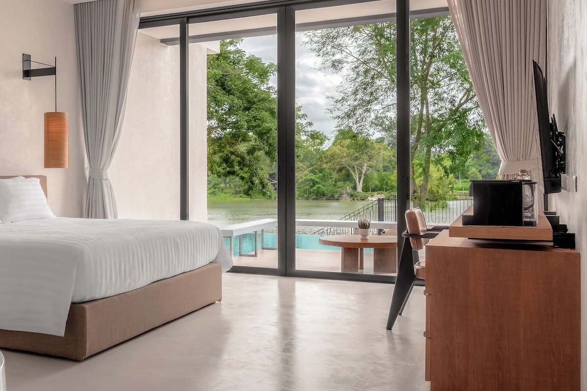 A modern bedroom with a large bed, a bathtub, and a view of a lake.