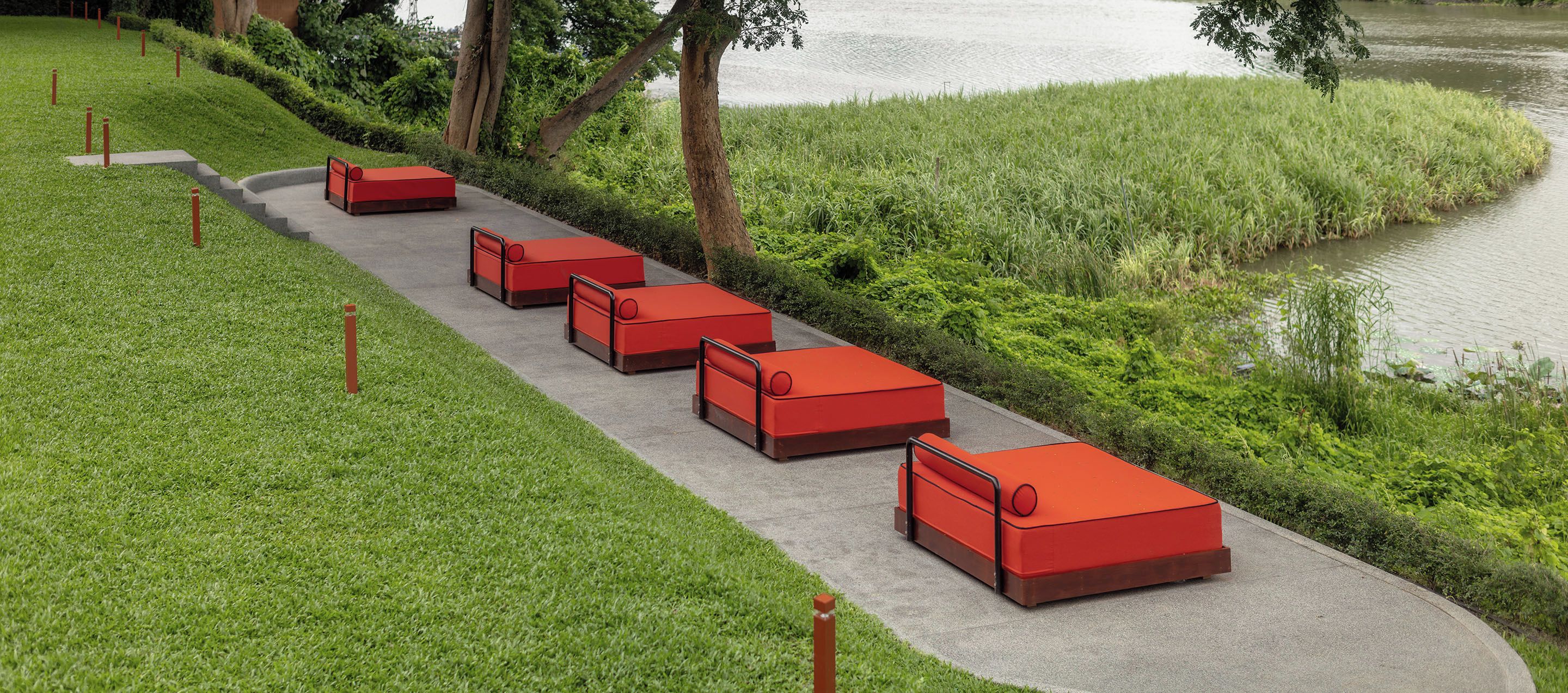 A row of red outdoor seating along a paved path beside a body of water.