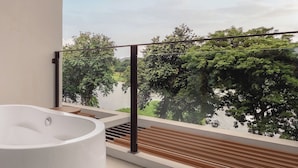 A modern bathroom with a freestanding bathtub, a wooden deck, and a view of a lake and trees. - Hykyo River Kwai Hotel (Kanchanaburi)