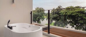 Een moderne badkamer met een vrijstaand bad, een houten terras en uitzicht op een meer en bomen.