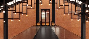 A modern interior with a brick wall, a central elevator, and a glass corridor.