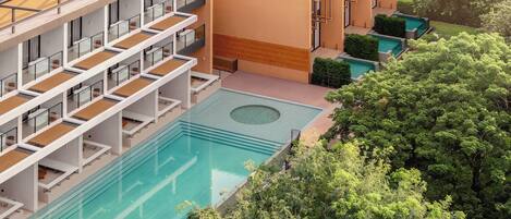 Un hotel de varios pisos con piscina, balcones y jardín.