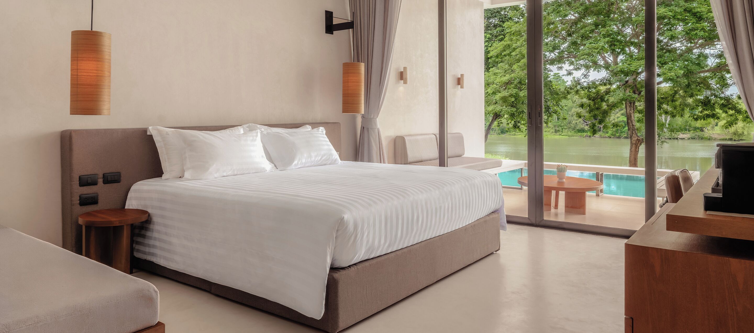 A hotel room with a bed, bedside tables, a TV, and a view of a swimming pool and greenery.