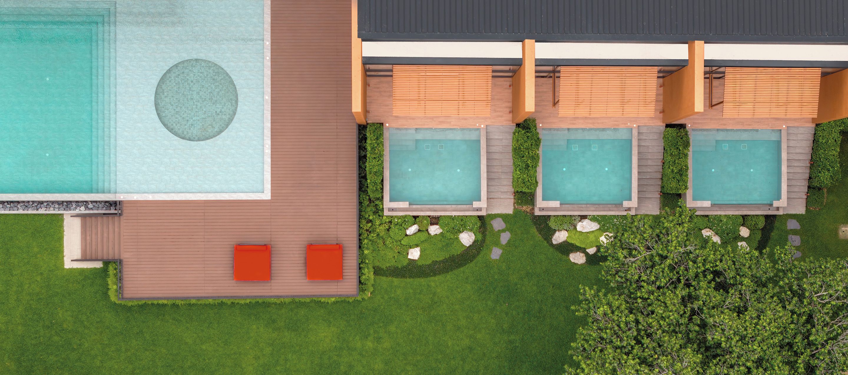 An aerial view of a resort with a large swimming pool, multiple hot tubs, and a well-maintained lawn.