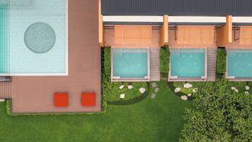 An aerial view of a resort with a large swimming pool, multiple hot tubs, and a well-maintained lawn.