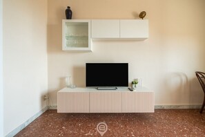 A modern living room with a flat-screen TV on a white console, a small plant, and a decorative item on the shelf above. - Casa Lelia – A special view in the heart of Cagliari 🌅✨ (Cagliari)