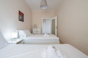 A hotel room with two beds, a bedside table with a lamp, a mirror, and a painting on the wall. - Casa Lelia – A special view in the heart of Cagliari 🌅✨ (Cagliari)