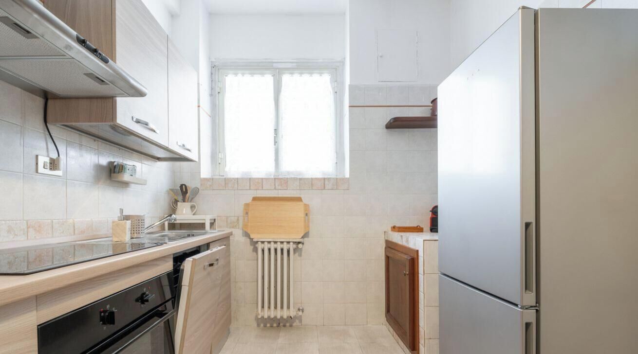 A compact kitchen with a built-in oven, a refrigerator, and a window providing natural light.