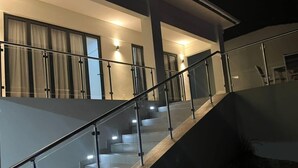 Una escalera moderna con barandillas de vidrio y una barandilla de madera que conduce a un rellano en el segundo piso con barandilla de vidrio.