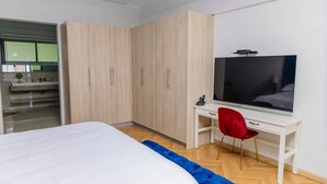 Un dormitorio con cama, televisor, escritorio con silla y armario.