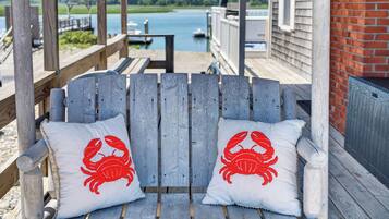 A wooden bench with two white cushions featuring red crab designs, overlooking a body of water with boats and a dock.