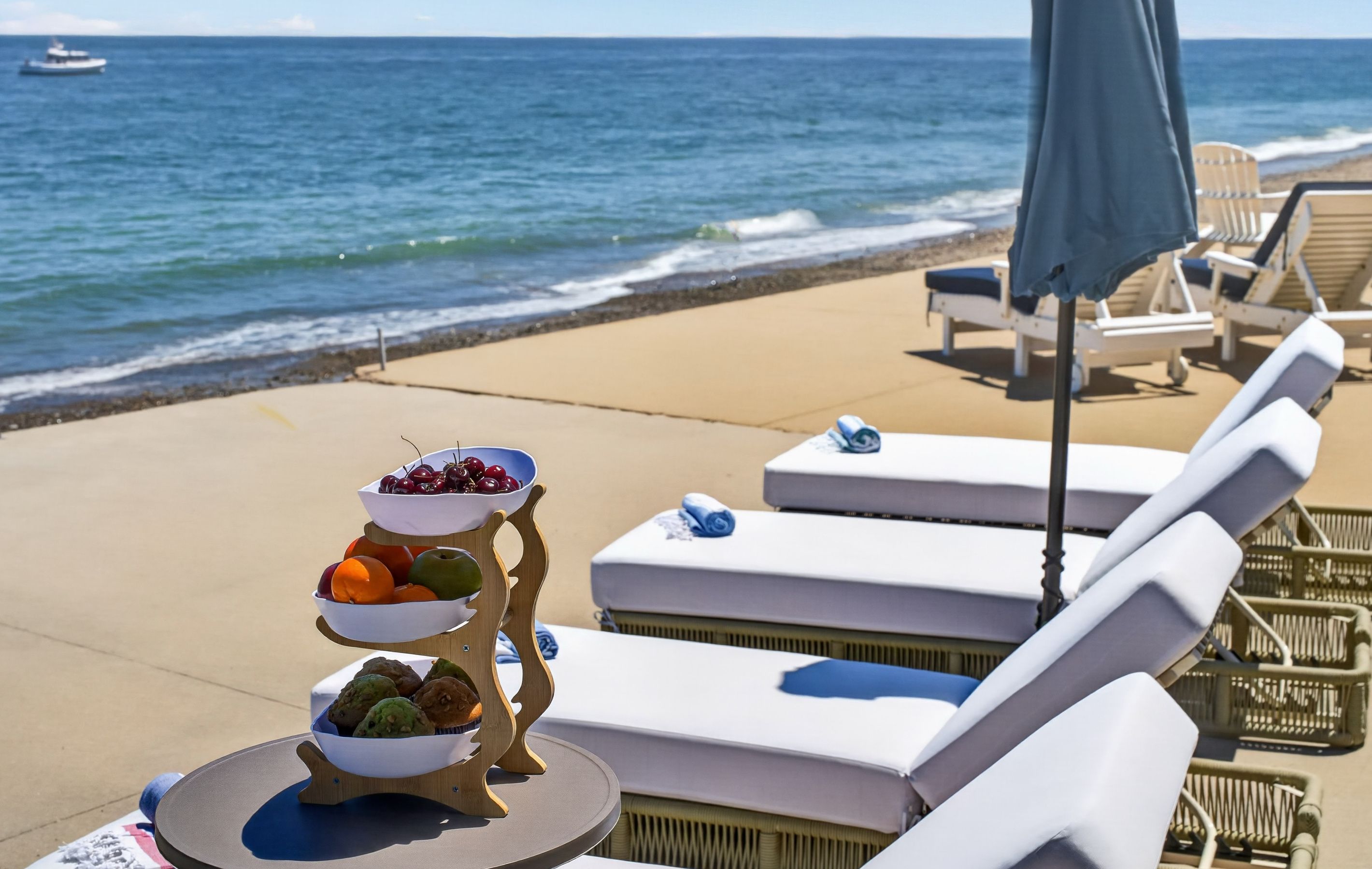 Un área de descanso frente a la playa con tumbonas, una mesa con frutas y vista al océano.