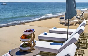 A beachside lounge area with sun loungers, a table with a fruit display, and a view of the ocean. - Ocean Views w/HotTub, Game Room, Movie Theater (Scituate)