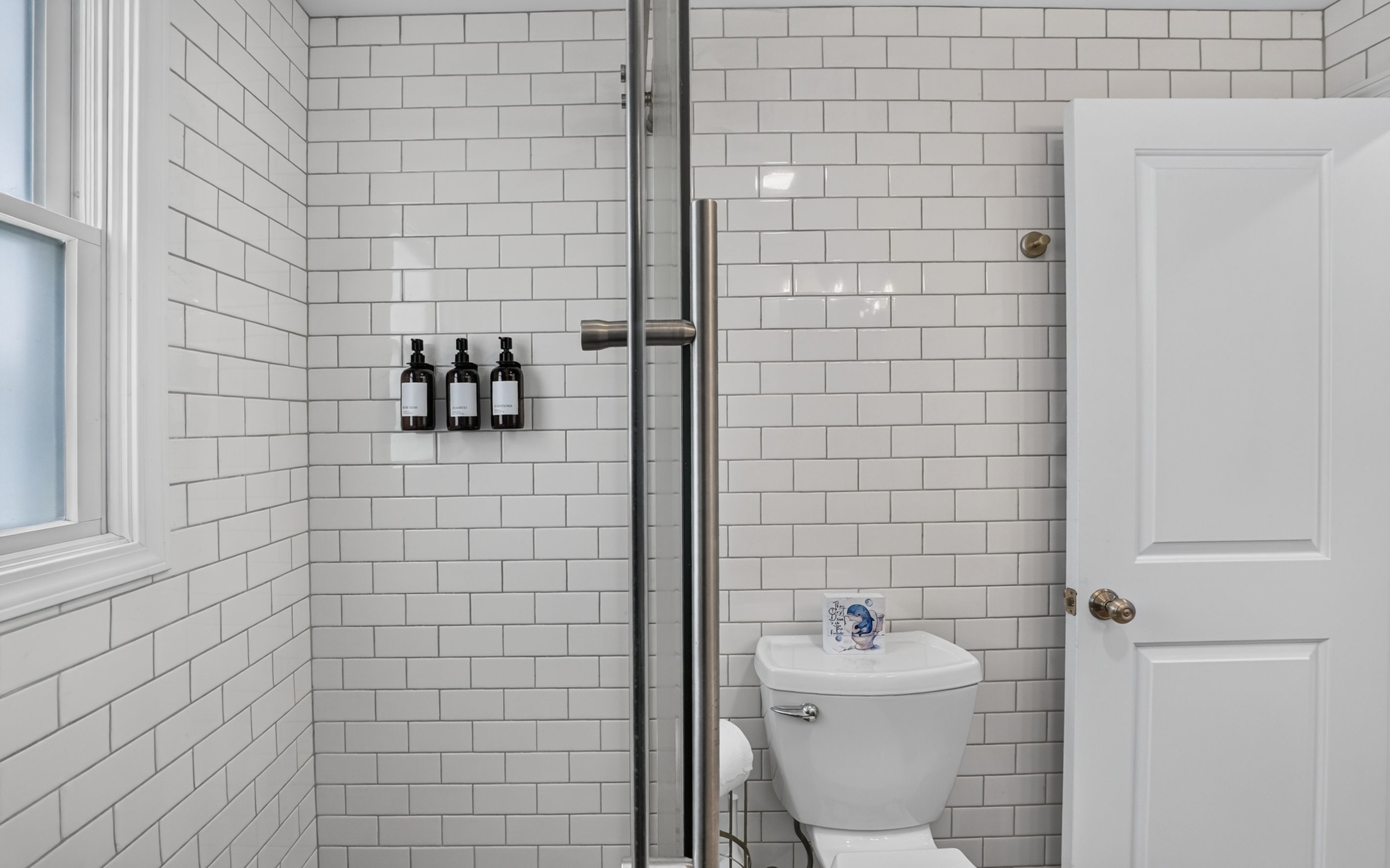 A bathroom with white subway tiles, a glass shower enclosure, and a toilet with a paper towel holder.