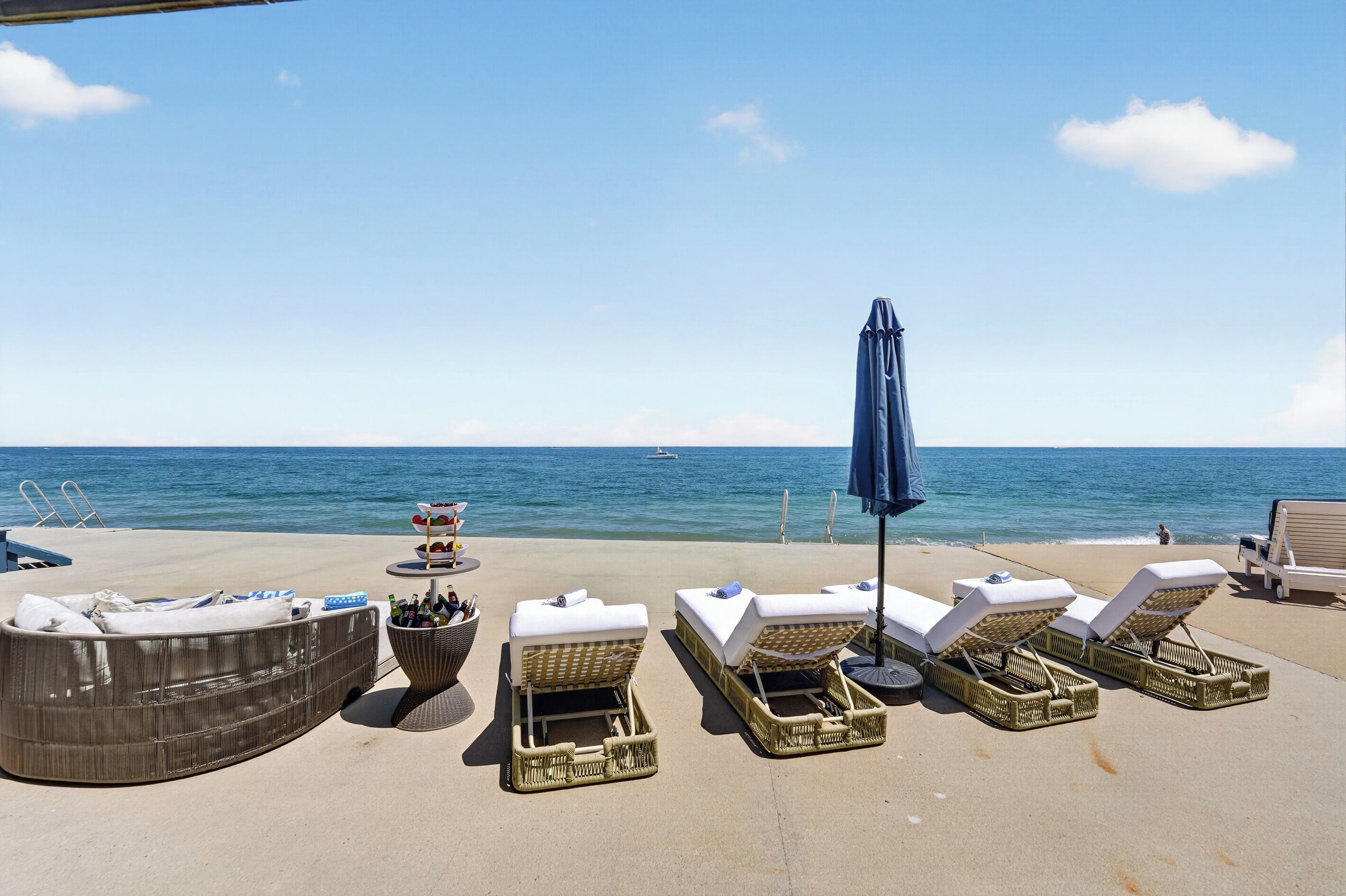 Et loungeområde ved stranden med liggestole, et bord med drikkevarer og udsigt til havet.