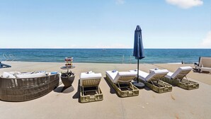 Uma área de descanso à beira-mar, com espreguiçadeiras, uma mesa com bebidas e vista para o oceano.