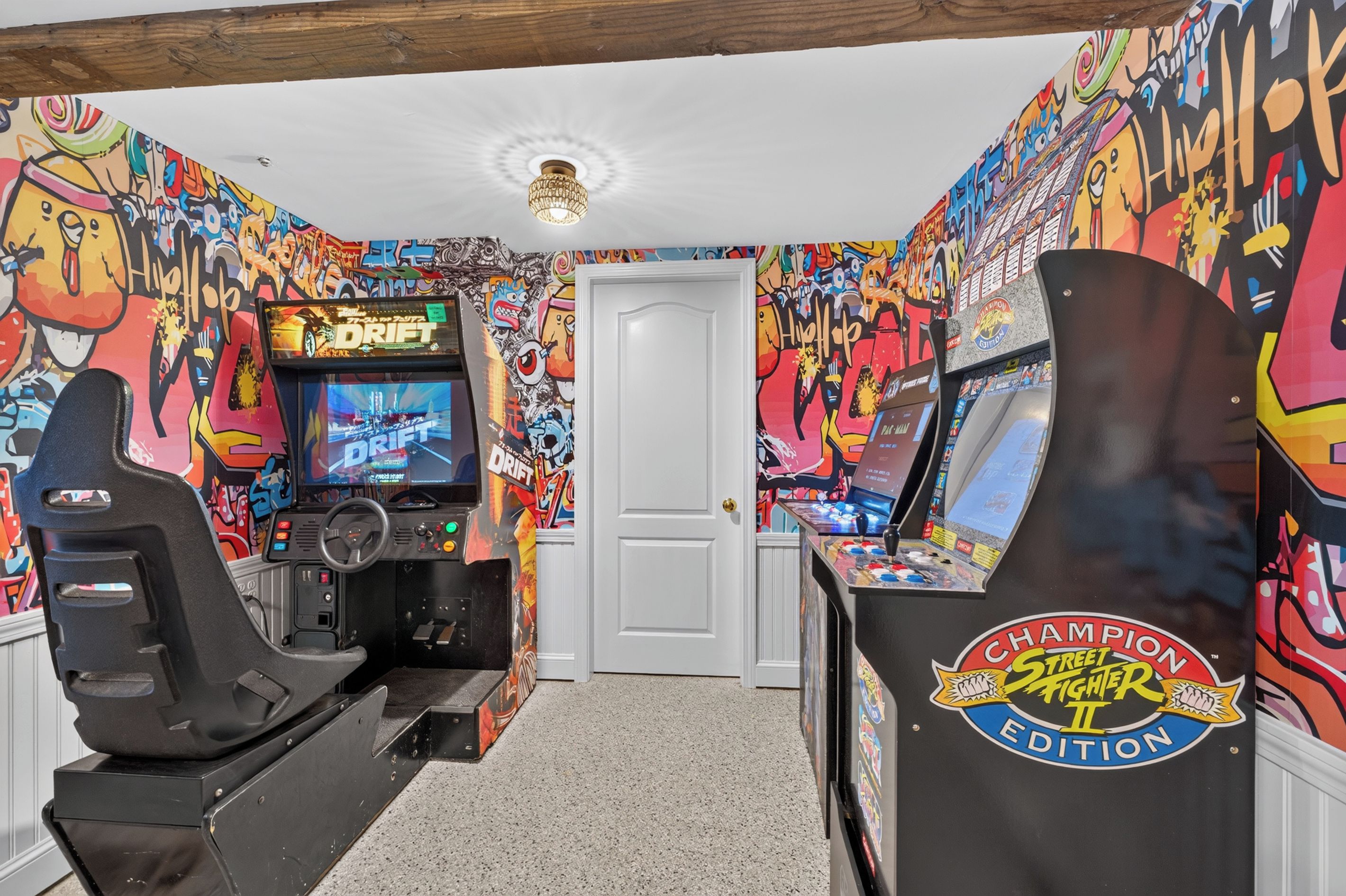 A gaming room with two racing simulators, a wall-mounted screen, and graffiti art.