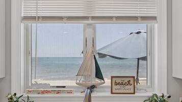 A window with a view of the ocean, a small sailboat model, and a sign that reads 'The beach is my happy place.'