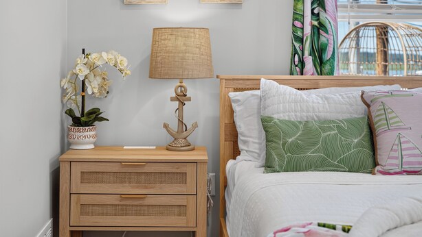 Quarto com mesa de cabeceira de madeira, luminária, orquídea em vaso e cama com almofadas estampadas.