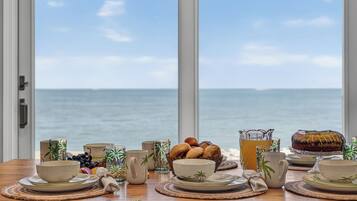 A dining table with various dishes and drinks, set against a view of the sea.