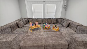 Um amplo sofá modular em um quarto com paredes brancas e uma janela com persianas.