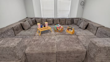 En stor modulsofa i et rum med hvide vægge og et vindue med persienner.
