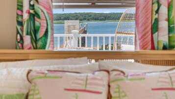 Blick aus einem Fenster auf ein Holzdeck, Geländer in Weiß sowie einen See und einen Wald.