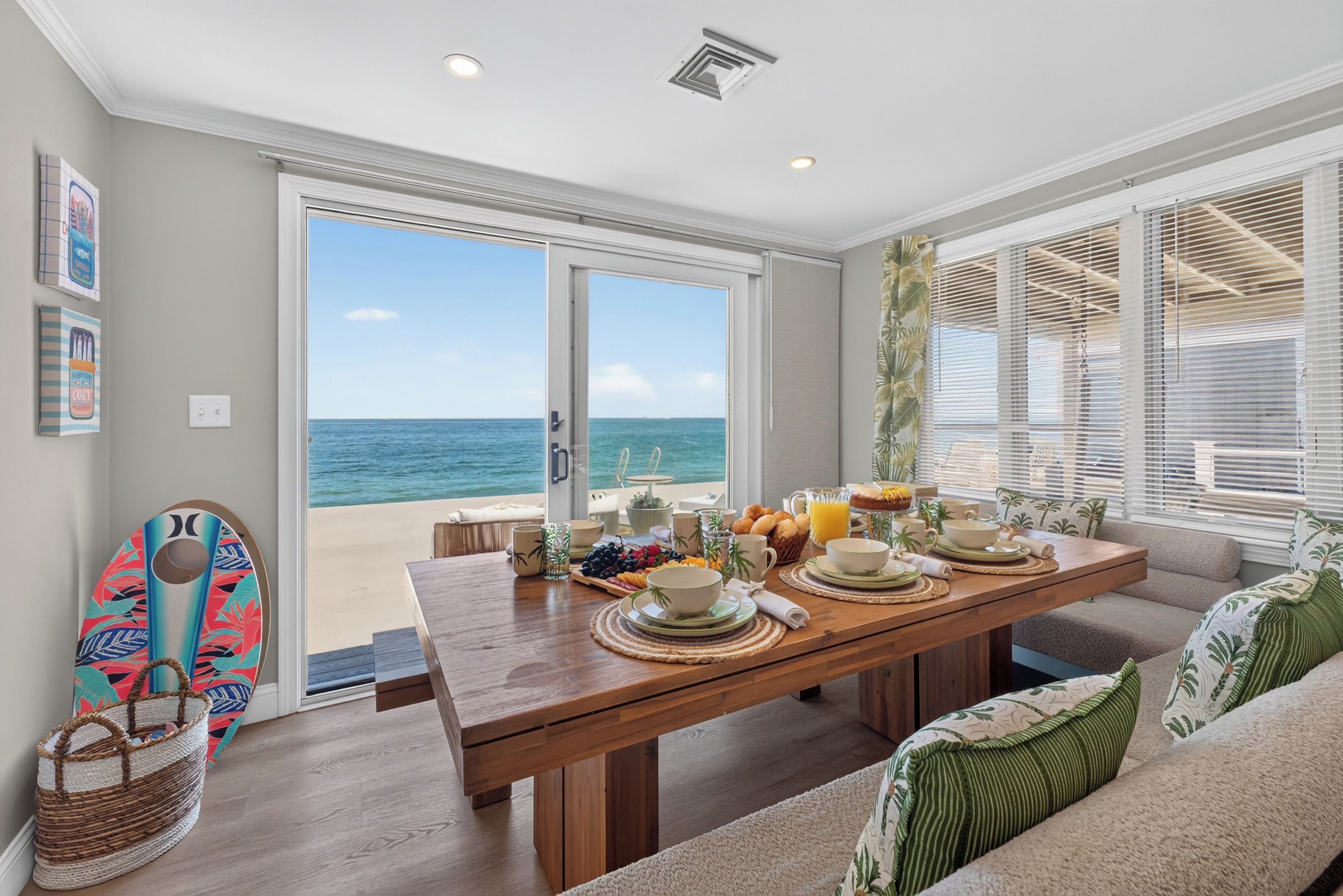 Un comedor con vistas al océano, una mesa de madera dispuesta para el desayuno y una zona de estar junto a la playa.