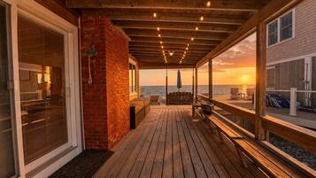 A wooden deck with a brick wall, a swing, and a view of the sunset over the water.