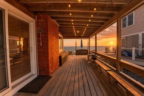 Um deck de madeira com muro de tijolos, um balanço e vista do pôr do sol sobre a água.