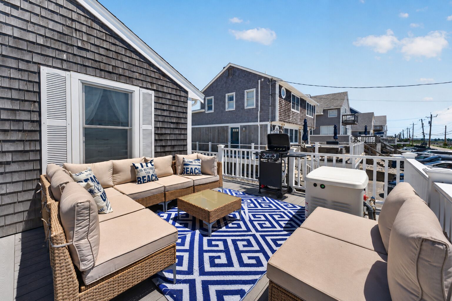 A covered outdoor seating area with a sofa, cushions, and a patterned rug.