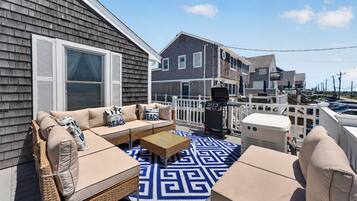 A covered outdoor seating area with a sofa, cushions, and a patterned rug.
