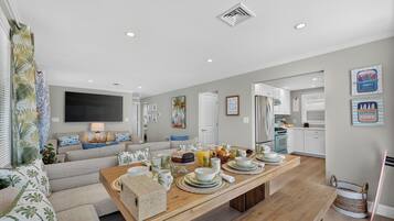 A modern living room with a sofa, a dining table set for breakfast, and a kitchen in the background.