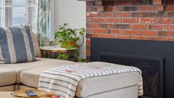 A living room with a sectional sofa, a fireplace, and a painting of colorful objects.