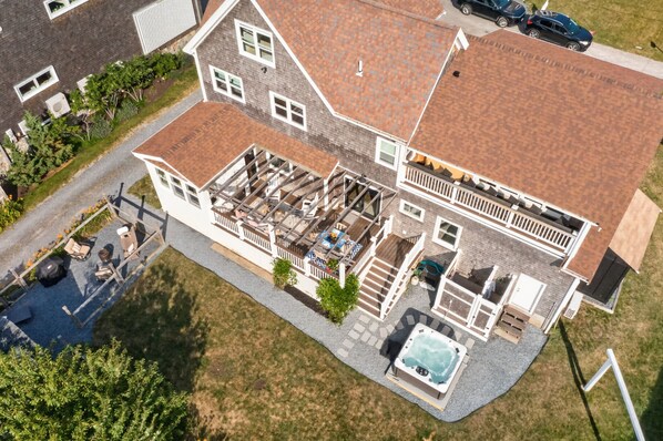 A two-story house with a large deck, a hot tub, and a covered outdoor seating area.