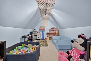 A child's playroom with a ball pit, a doll, a bookshelf, and a small house.