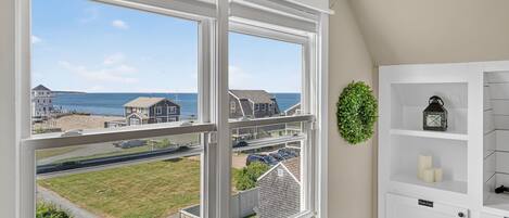 A room with a large window offering a view of the sea and neighboring houses.