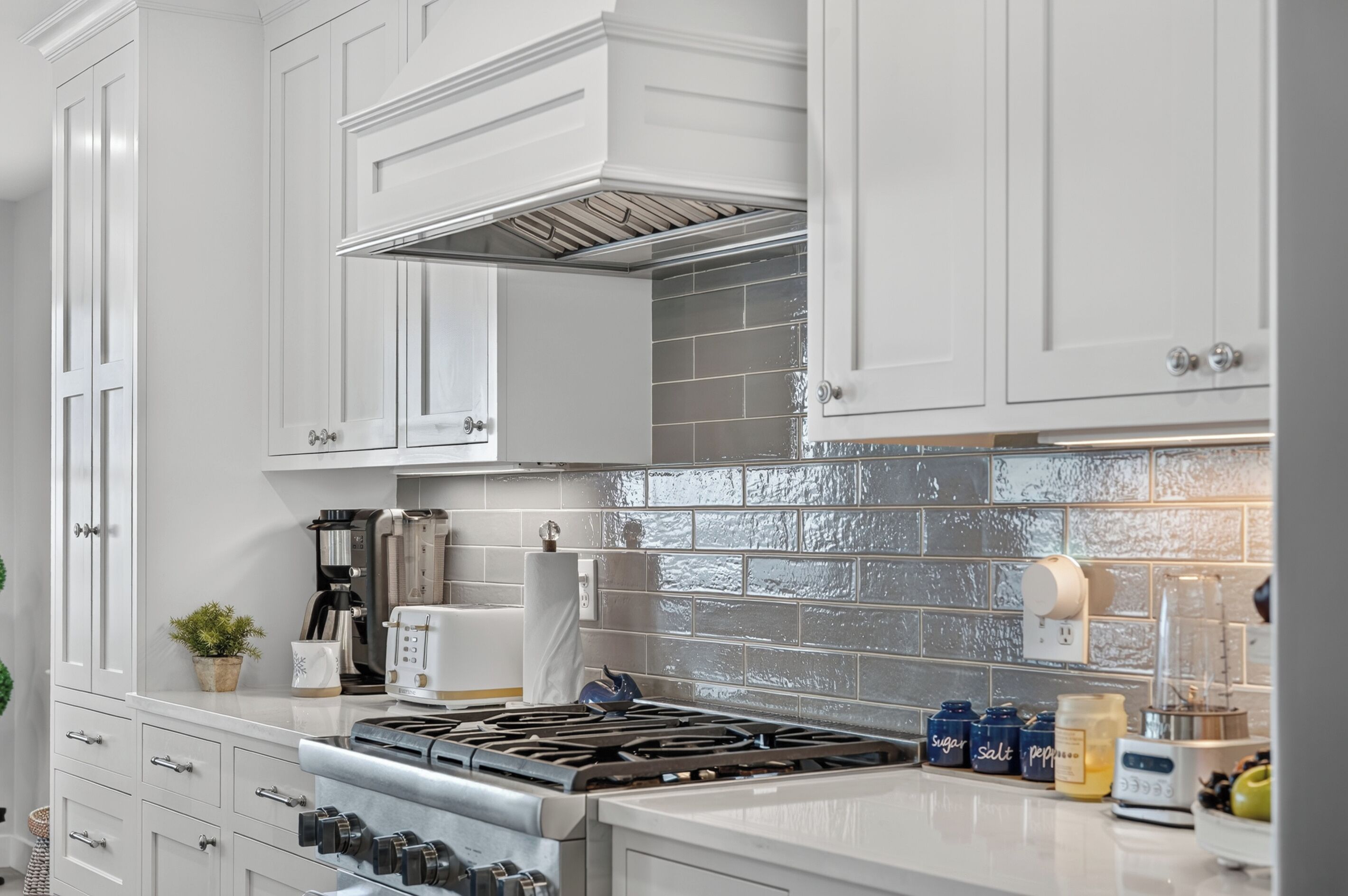 A kitchen with white cabinetry, a gas stove, a coffee maker, and a tiled backsplash.