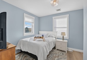 A bedroom with a bed, bedside table, lamp, and a TV on a stand.