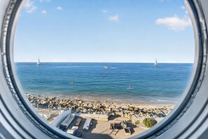Vista d'una platja amb cel blau, costa rocosa i zona de relaxació amb gandules.