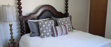 A bed with a wooden headboard, multiple pillows, a bedside lamp, and a wooden door.