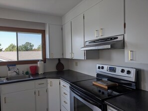 Eine Küche mit weißen Schränken, einer schwarzen Arbeitsplatte, einem Edelstahlherd und einem Fenster mit Blick auf Bäume.