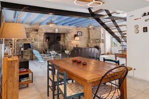 A dining area with a wooden table and chairs, a stone fireplace, and a staircase. - Characterful House in the Gulf of Morbihan with Private Terrace and Garden (Sarzeau)