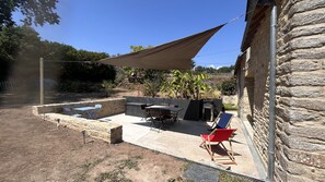 Un patio al aire libre con mesa y sillas, una parrilla y una zona con sombra.