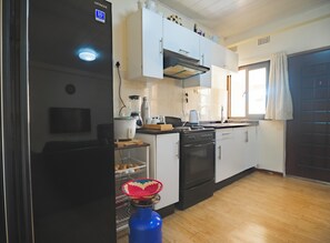 A compact kitchen with a black refrigerator, white cabinets, a gas stove, and a window with curtains. - Beautiful 2-bedroom apartment in gated and secure community (Lusaka)
