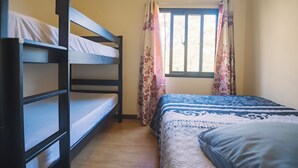 Um quarto com beliches, uma janela com cortinas florais e uma cama com colcha estampada.