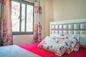 A bedroom with a bed, floral curtains, and a window. - Beautiful 2-bedroom apartment in gated and secure community (Lusaka)
