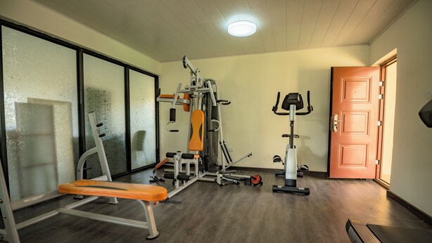 Uma academia com equipamentos de ginástica, um banco e uma porta.